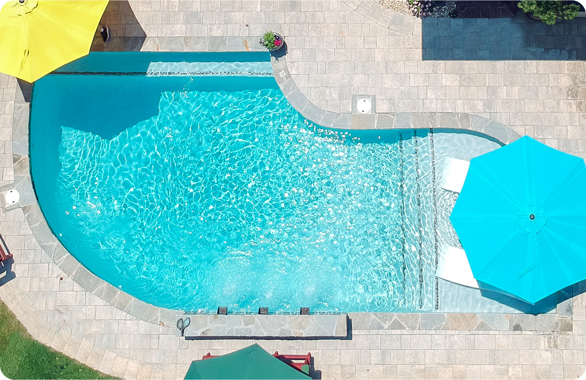 Gunite pool with tanning ledge with integrated patio umbrella and paver hardscape.